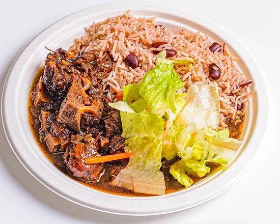 Braised oxtail in gravy with rice and peas and lettuce on a plate
